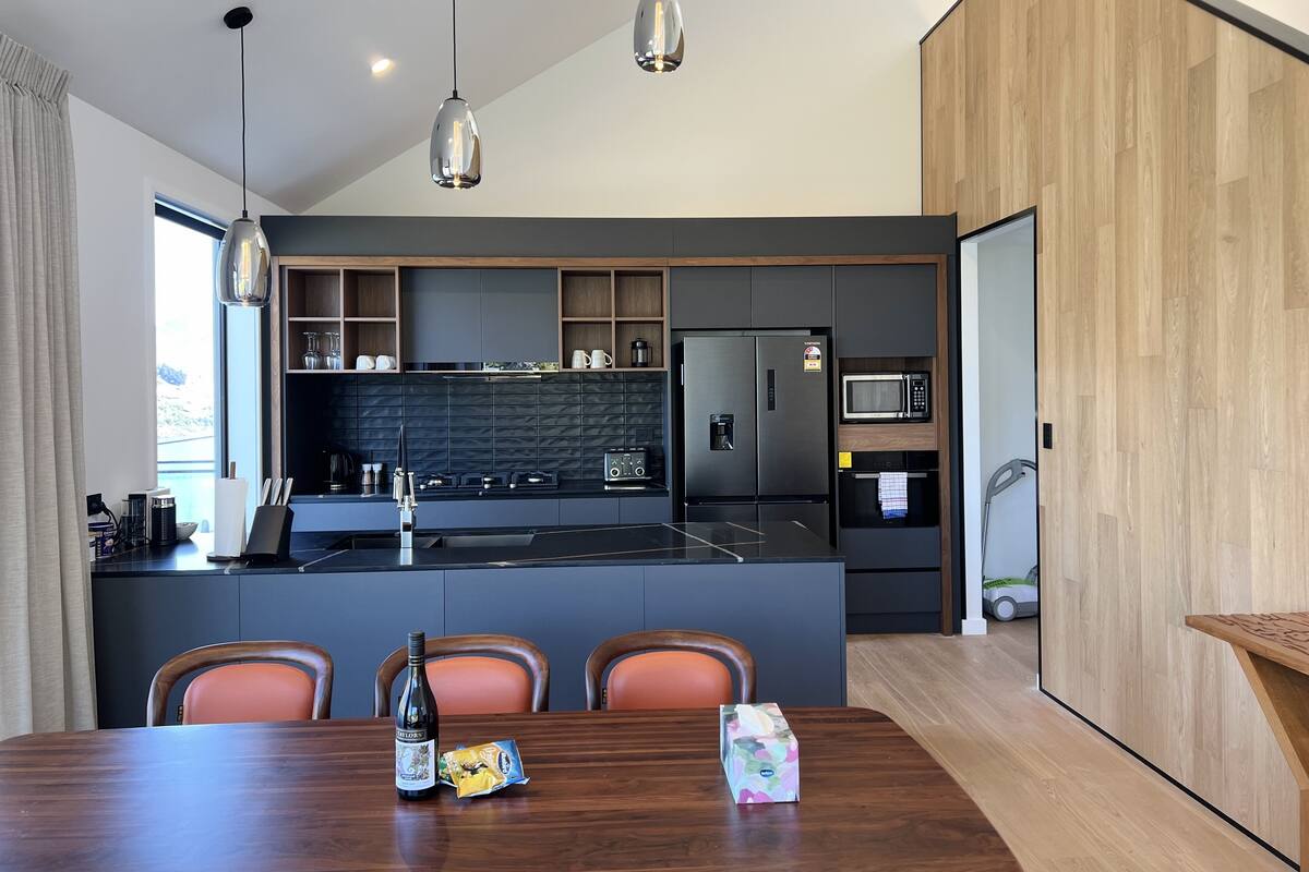 A modern kitchen with dark cabinetry, a central island, and a dining area with a wooden table.