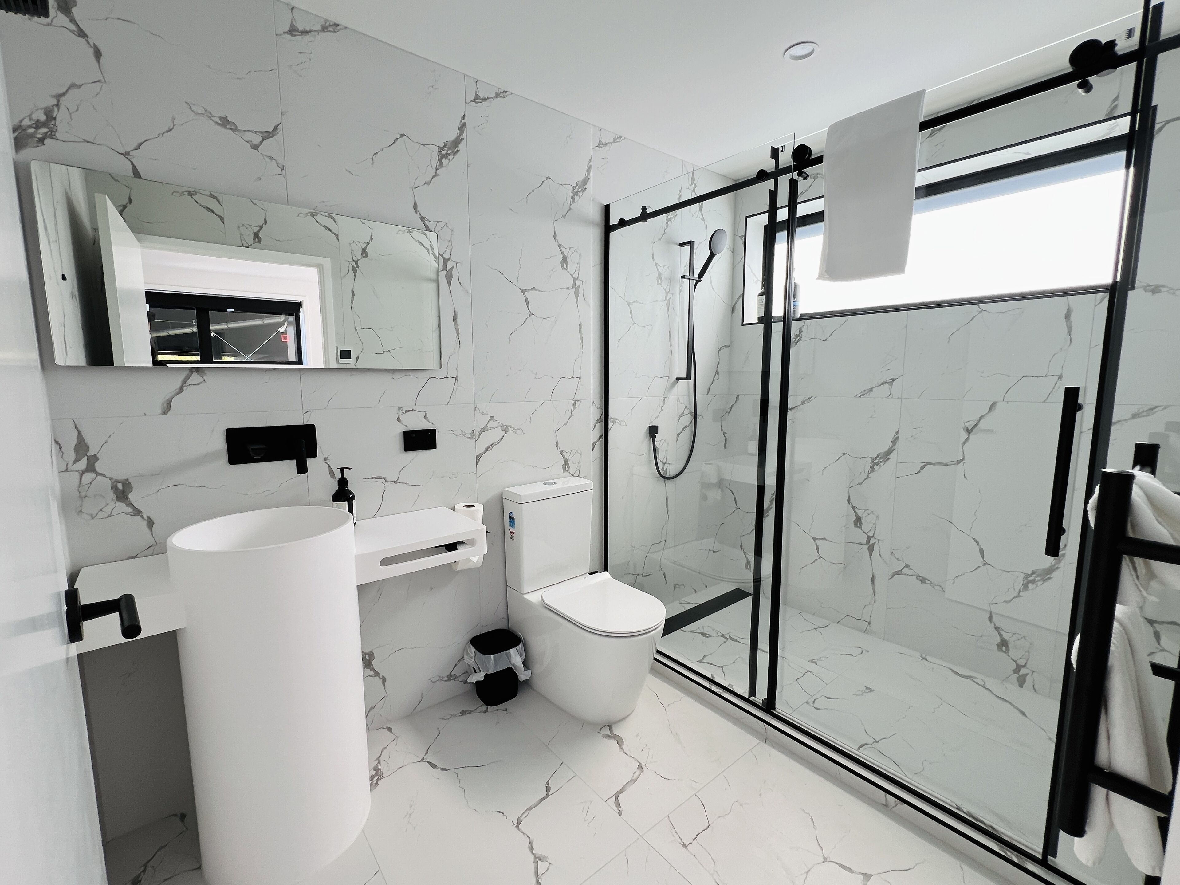 A modern bathroom with a large white sink, a toilet, and a glass-enclosed shower area.