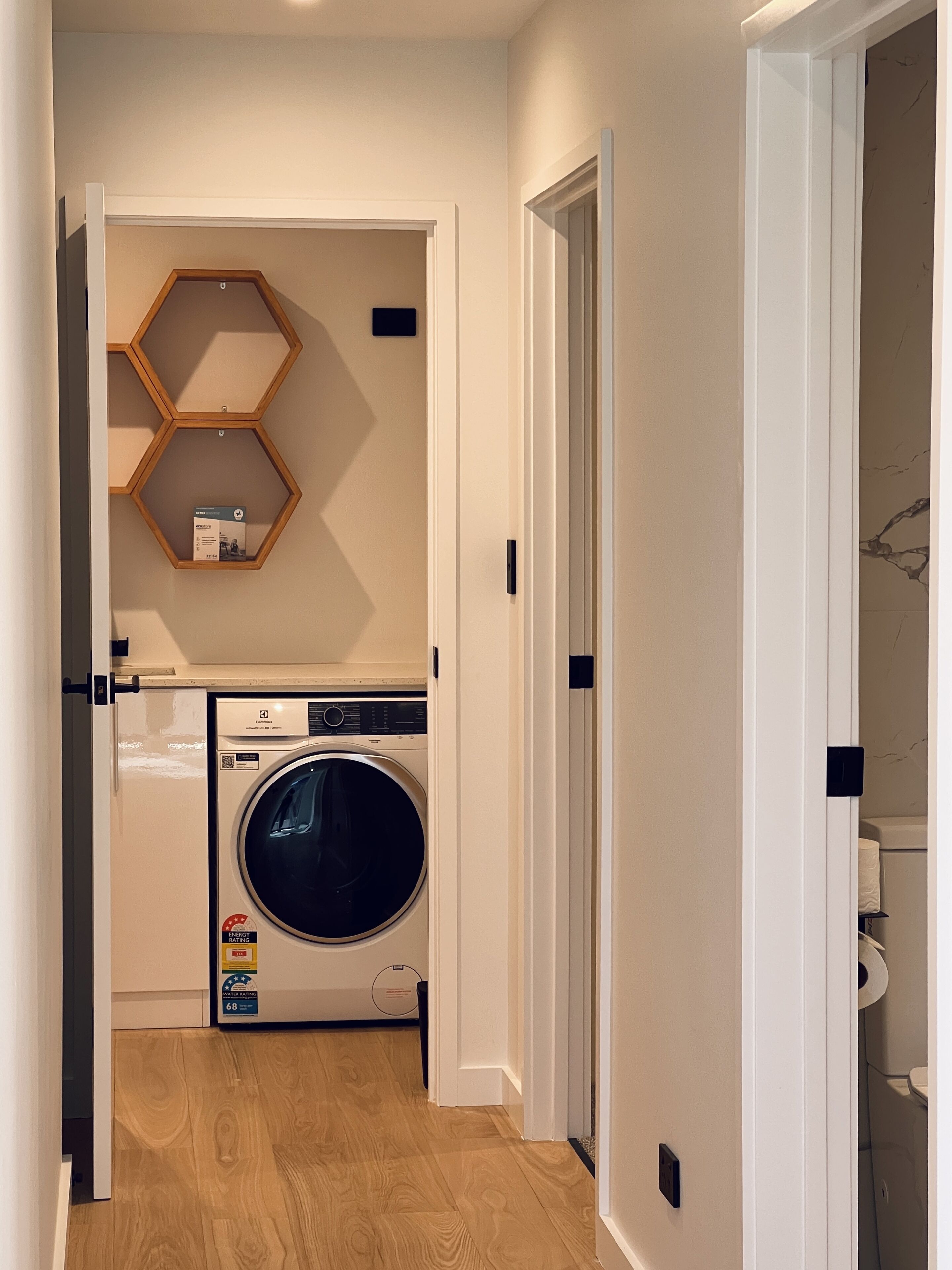 Een wasserette met een wasmachine, een droger en een houten plank met honingraatstructuur.