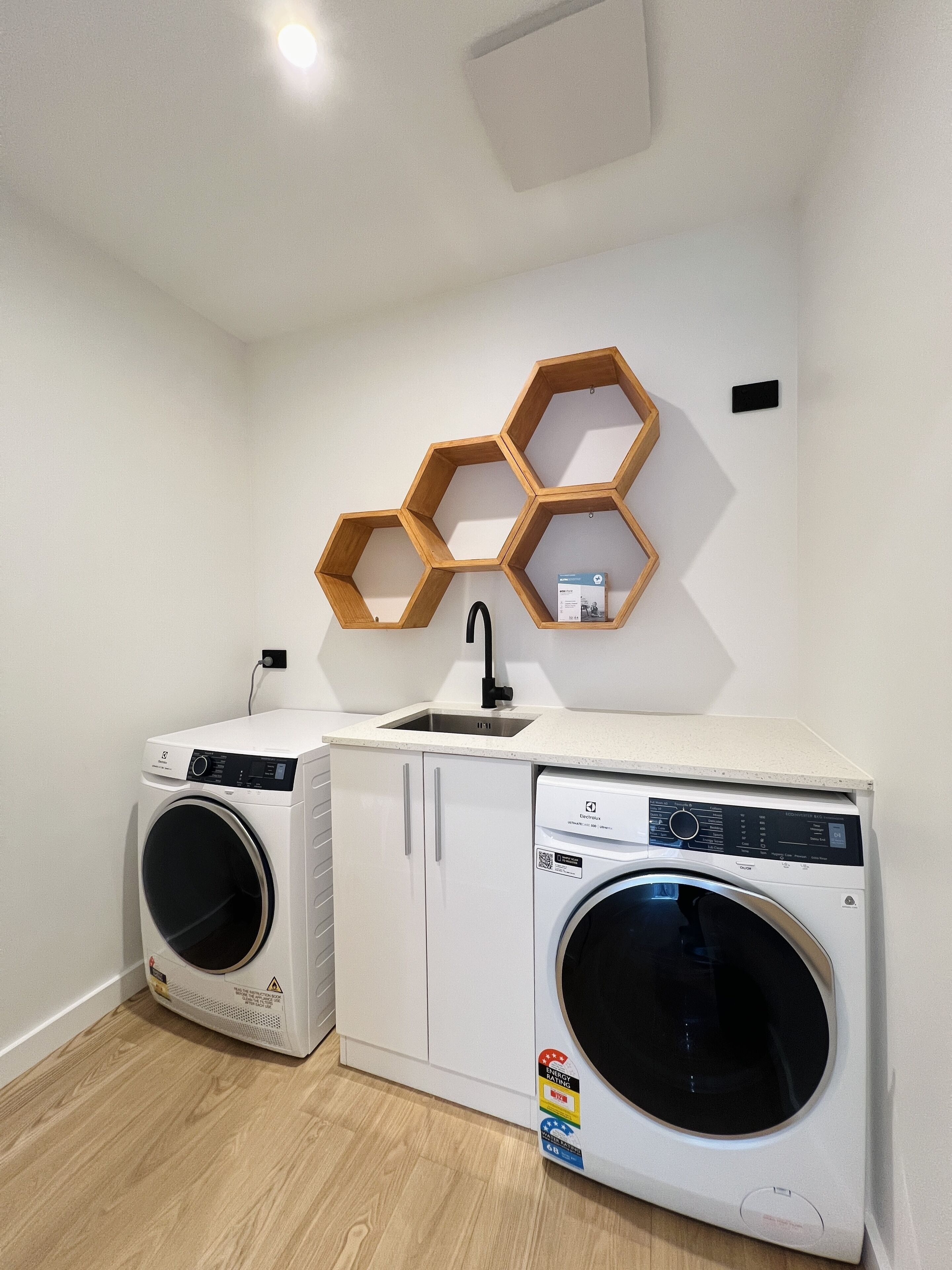 A laundry room with two washing machines, a sink, and wooden hexagonal shelves on the wall.