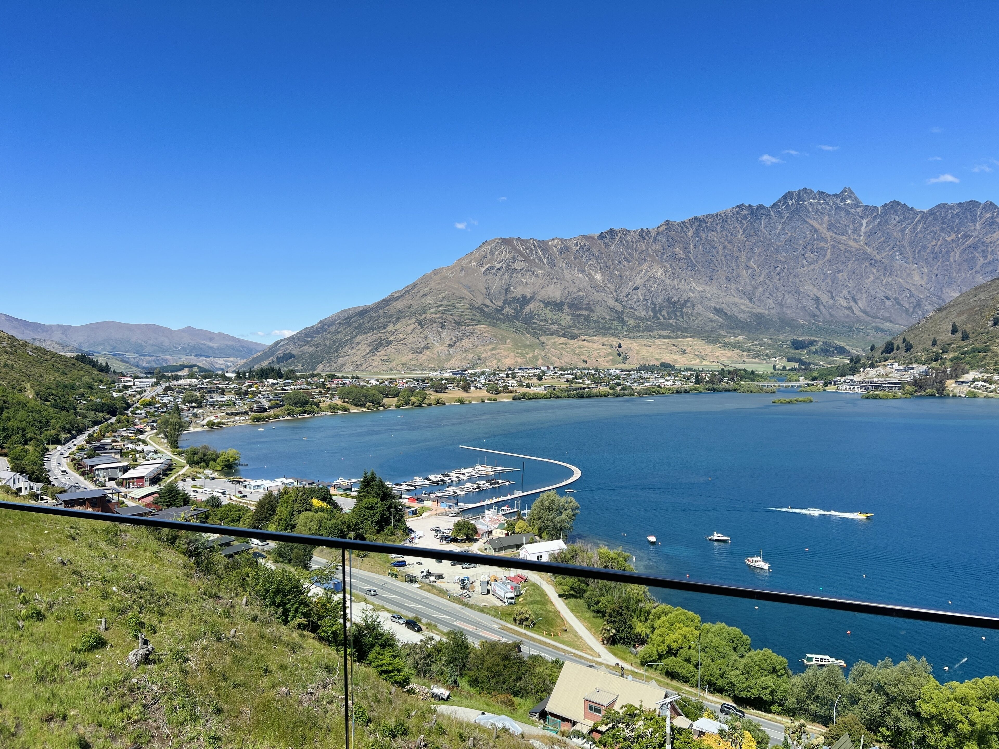 A coastal town with a marina, mountains in the background, and a clear blue sky.