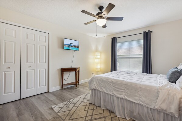 A bedroom with a bed, a ceiling fan, a TV, a lamp, and a window with curtains. - Beautiful Treasure Coast Gem w/ Heated Pool, Private Patio & BBQ Grill! 🌴 (Sebastian)