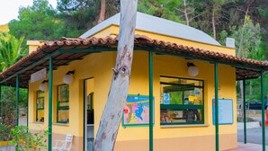 Un petit bâtiment jaune avec un toit en tuiles, un banc et une carte accrochée au mur.