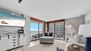 Een moderne woonkamer met een grote televisie, een bank, een salontafel en een balkon met uitzicht op zee.