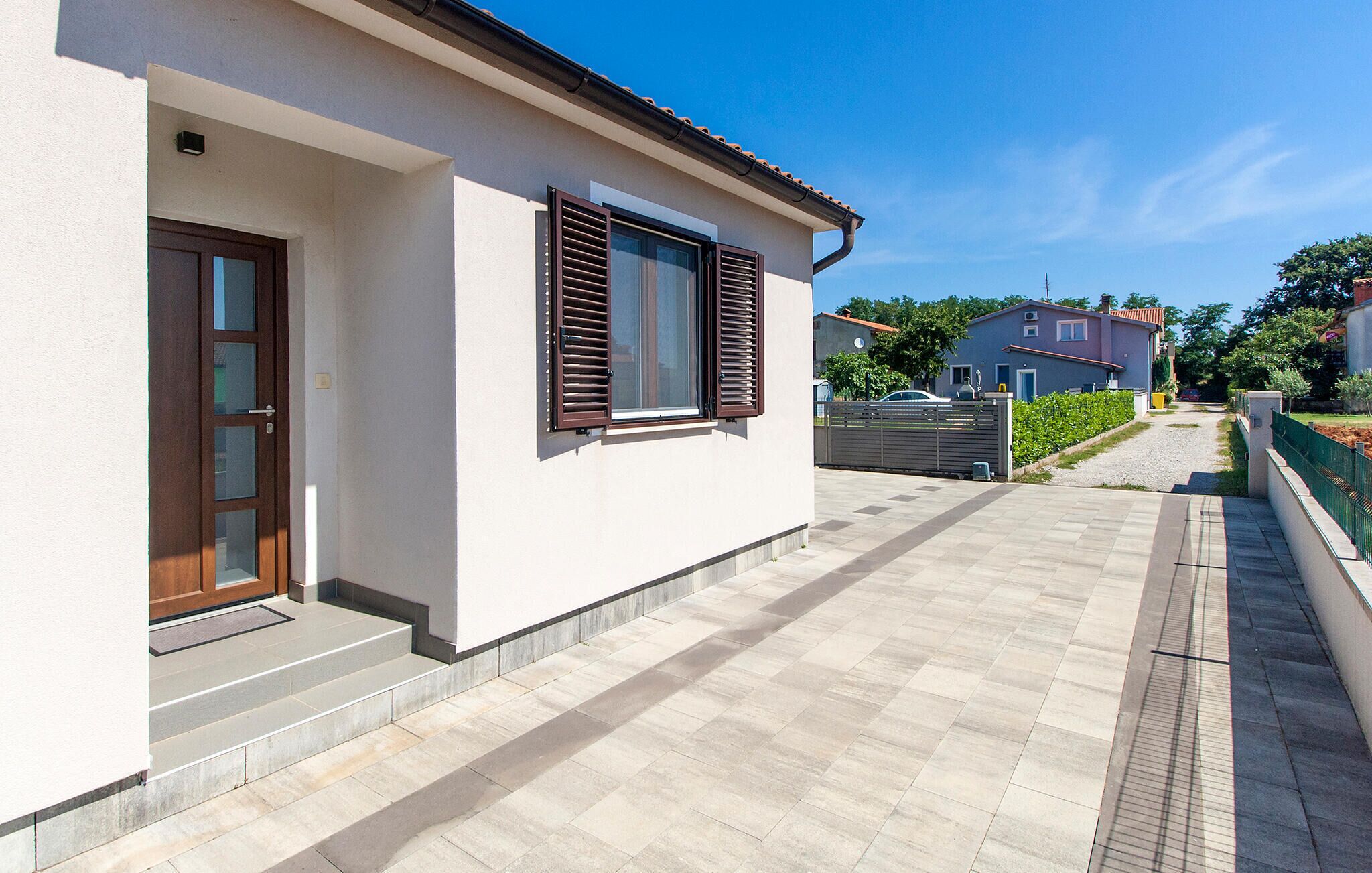 A modern house with a white exterior, a wooden door, and a window with brown shutters.