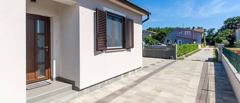 A modern house with a white exterior, a wooden door, and a window with brown shutters.