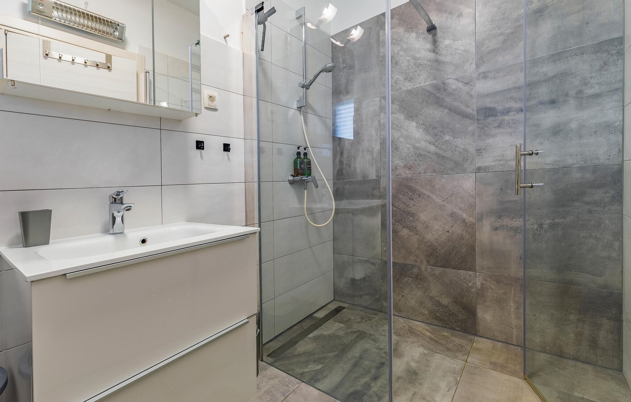 A modern bathroom with a white sink, a glass shower enclosure, and a mirror above the sink.