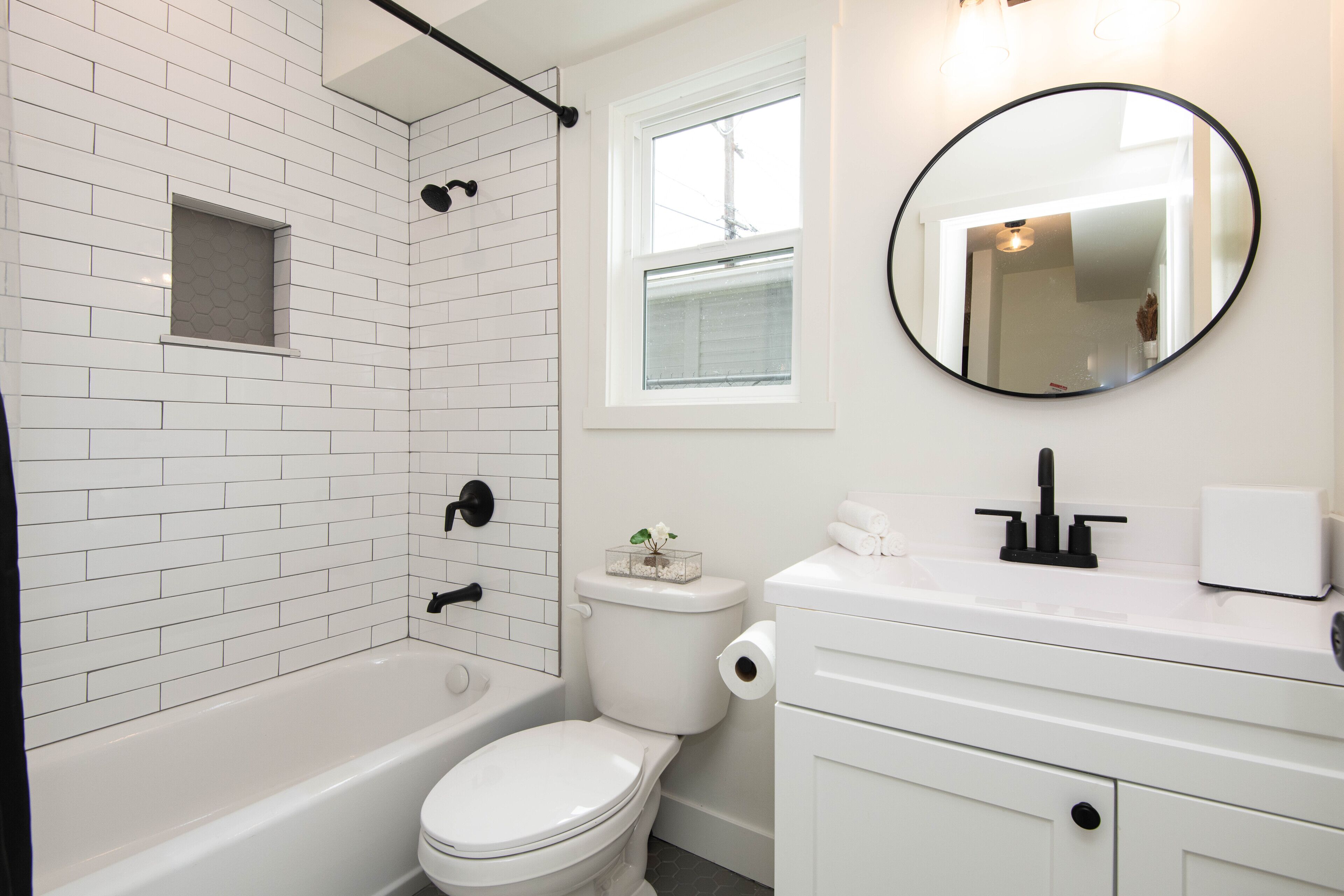 A bathroom with a white bathtub, toilet, and sink, a small window, and a mirror on the wall.