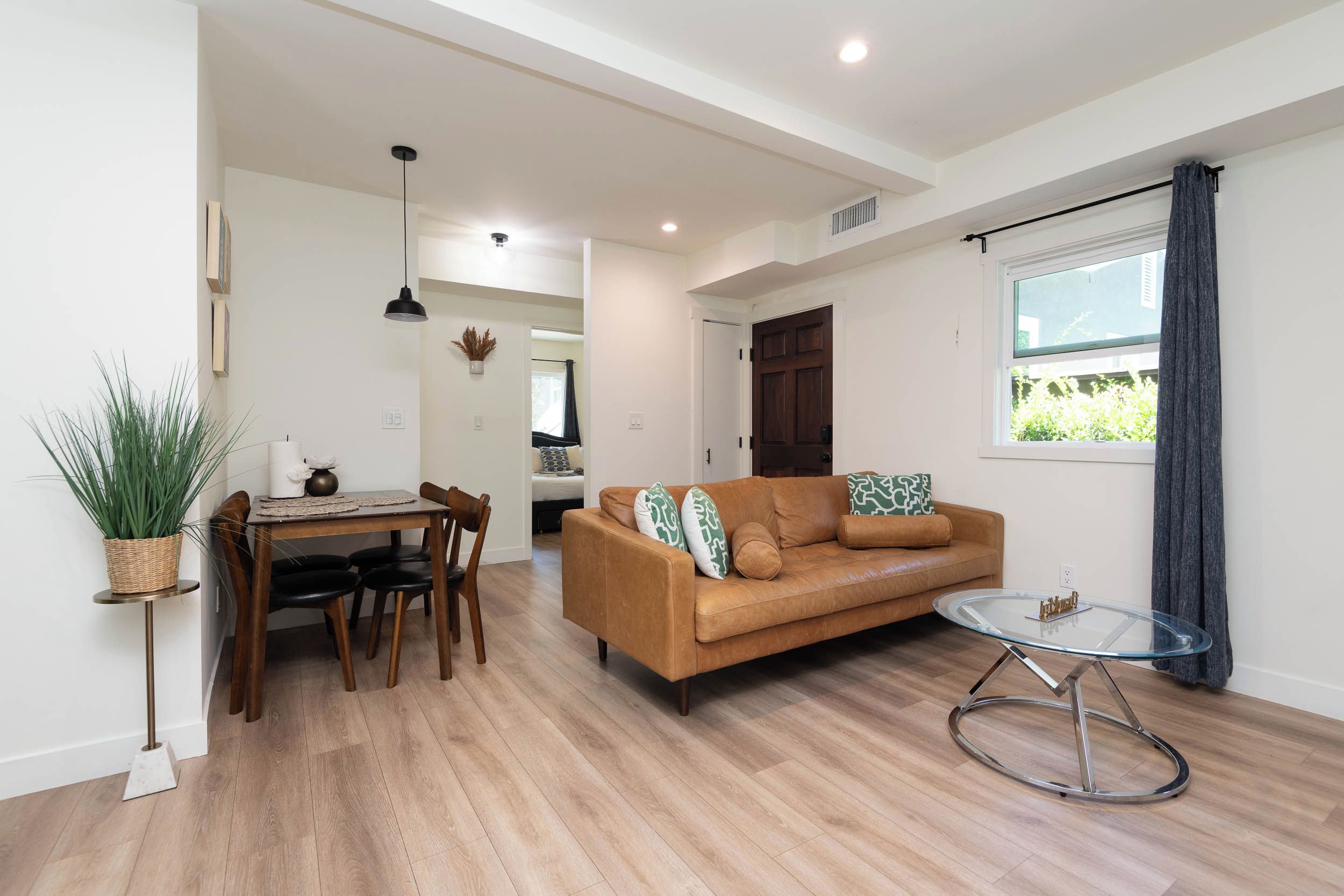 A modern living room with a brown leather sofa, a glass coffee table, and a dining area with a wooden table and chairs.