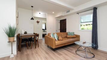 A modern living room with a brown leather sofa, a glass coffee table, and a dining area with a wooden table and chairs.