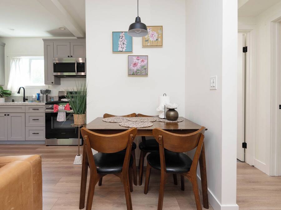 A modern kitchen with grey cabinets, a microwave, and a sink. There is a dining table with chairs and a vase with flowers.