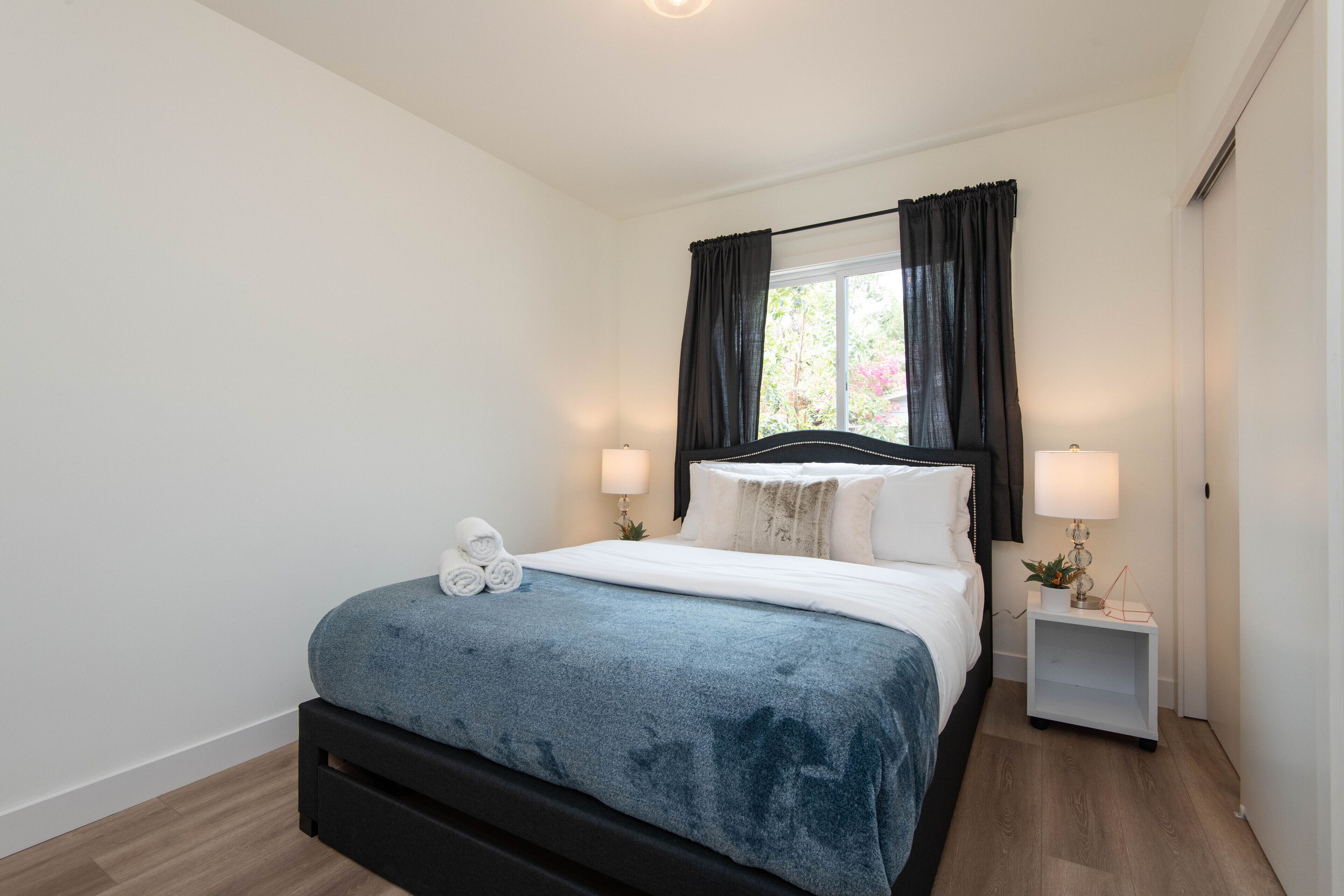 A neatly arranged bedroom with a bed, bedside lamps, and a window with curtains.