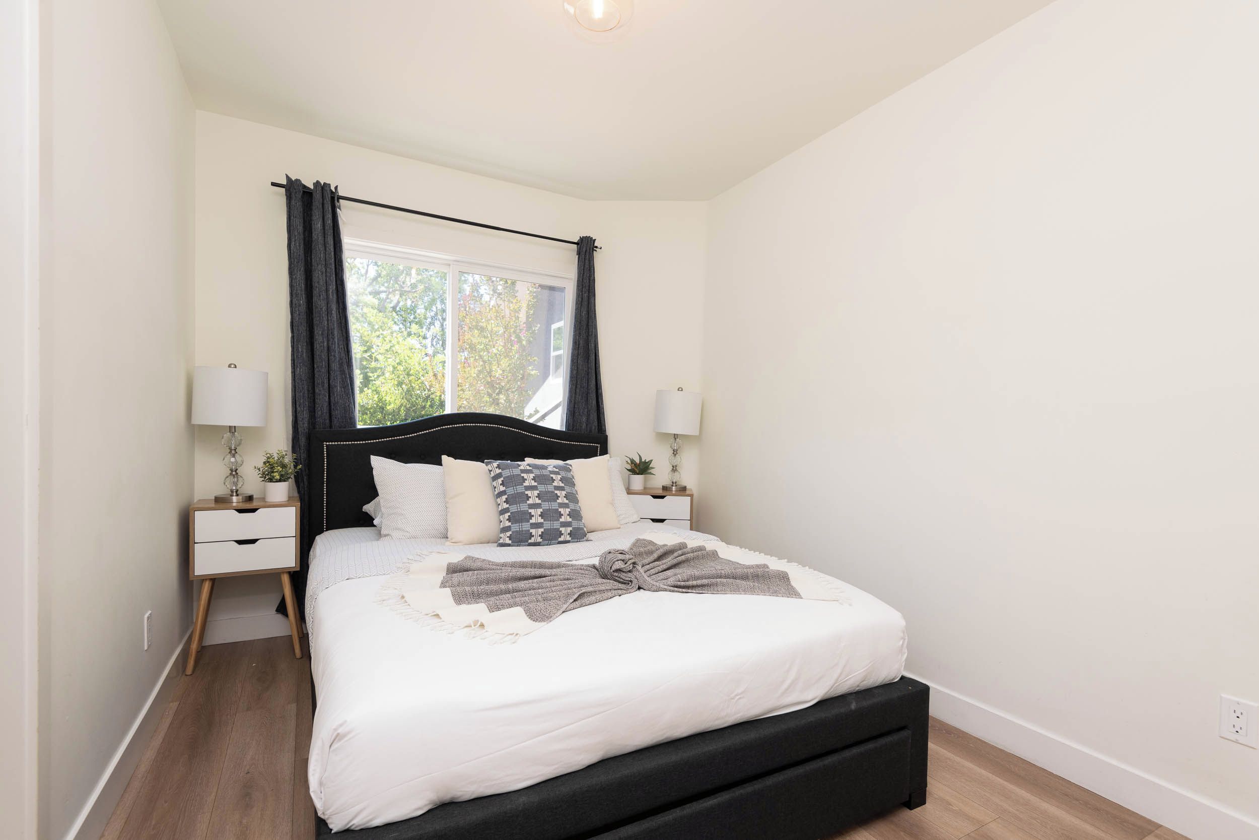 Une chambre à coucher avec un lit, des tables de chevet, une fenêtre avec des rideaux et une petite table de nuit avec une lampe.