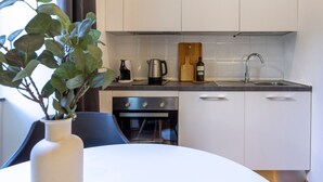 A modern kitchen with white cabinets, a stainless steel sink, a coffee maker, a kettle, and a wooden cutting board. - Ghiberti - Studio in the City Center (Trieste)