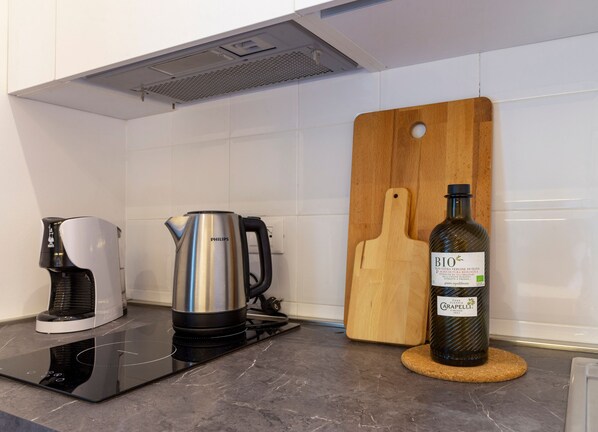 A kitchen with a coffee maker, a kettle, and a bottle of olive oil on the counter.