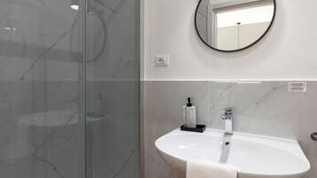 A modern bathroom with a glass shower enclosure, a round mirror, and a white sink with a towel.