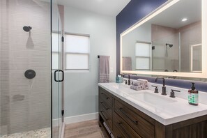 Une salle de bain moderne dotée d’une douche à parois de verre, d’un meuble-lavabo à deux vasques et d’un grand miroir.