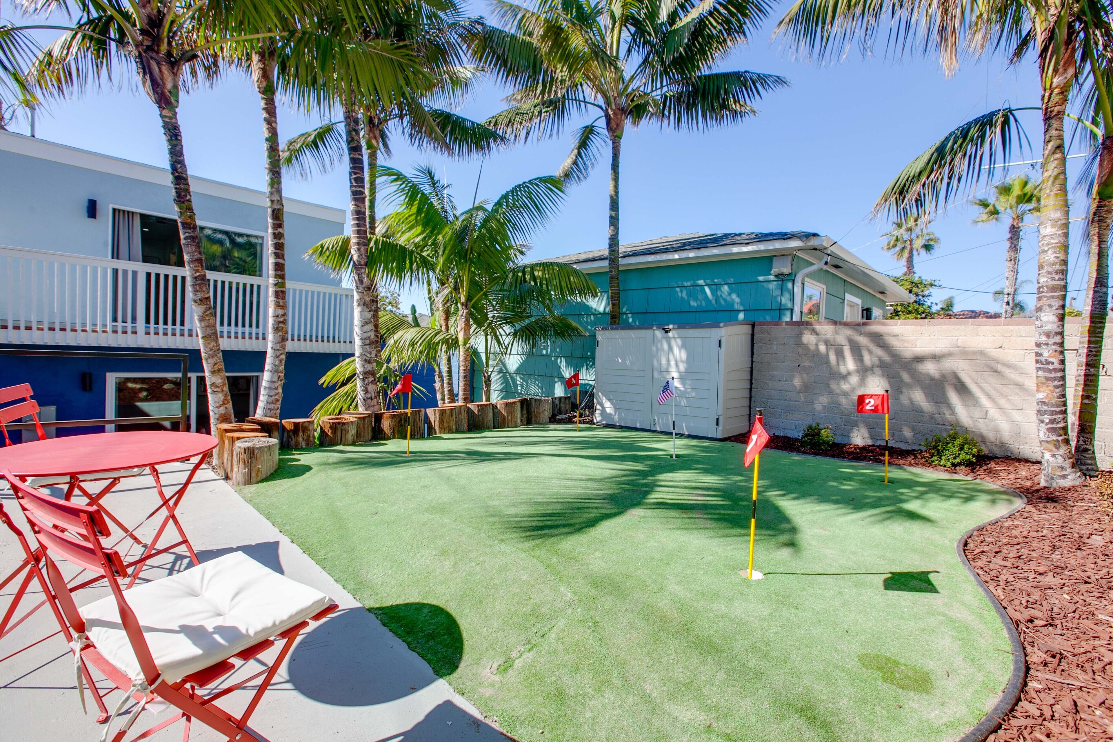 A pool table with a red table and white cushions, surrounded by palm trees and a building with a blue exterior.