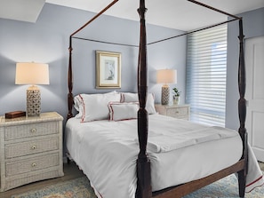 A four-poster bed with white bedding and red trim, flanked by two nightstands with lamps and a framed picture above.