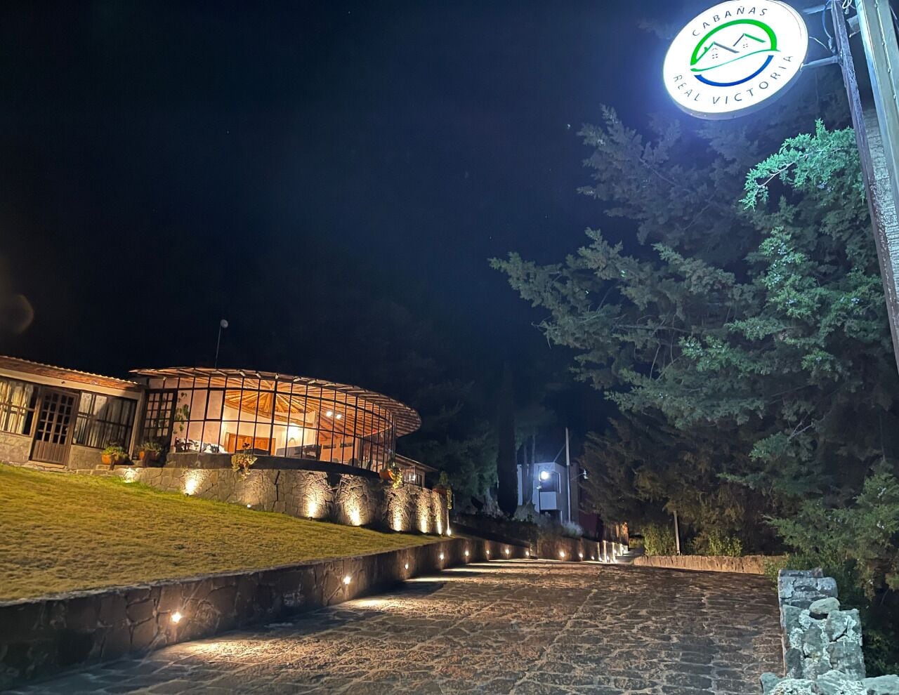 A well-lit building with a circular glass structure, surrounded by a stone pathway and greenery.