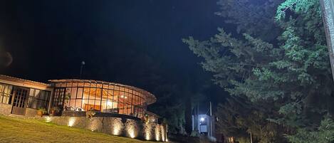 A well-lit building with a circular glass structure, surrounded by a stone pathway and greenery.