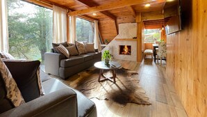 A cozy cabin interior with a sofa, a round coffee table, a fireplace, and a dining area. - Cabañas Real Victoria (El Oro de Hidalgo)
