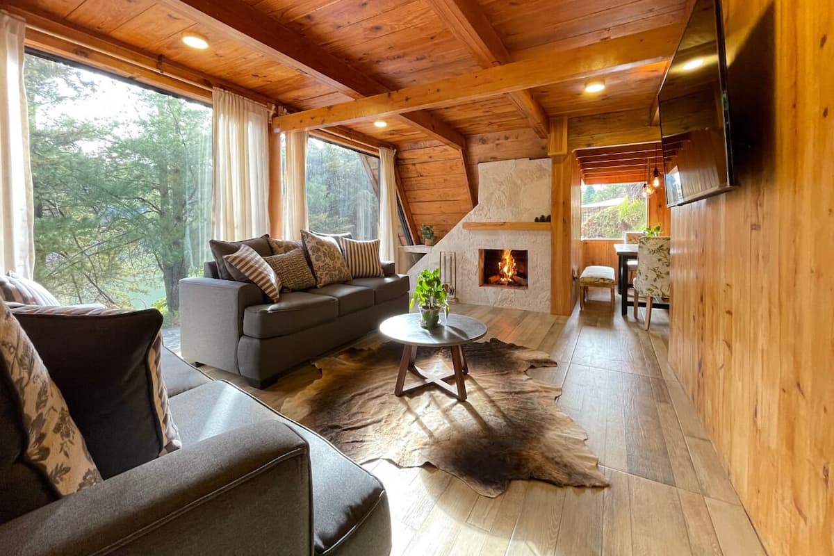 A cozy cabin interior with a sofa, a round coffee table, a fireplace, and a dining area.