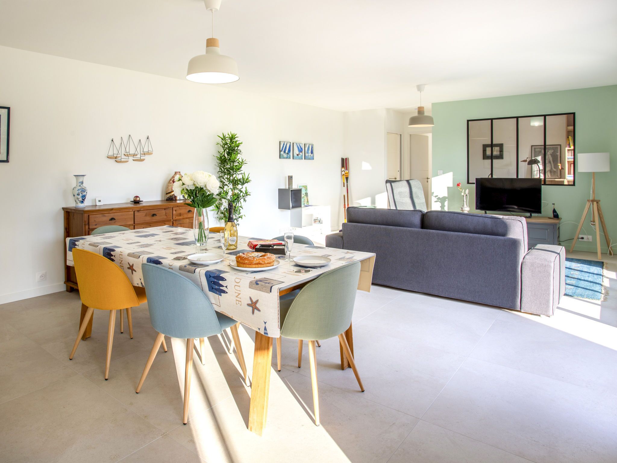 A modern living room with a grey sofa, a dining table with chairs, and a TV on a stand.