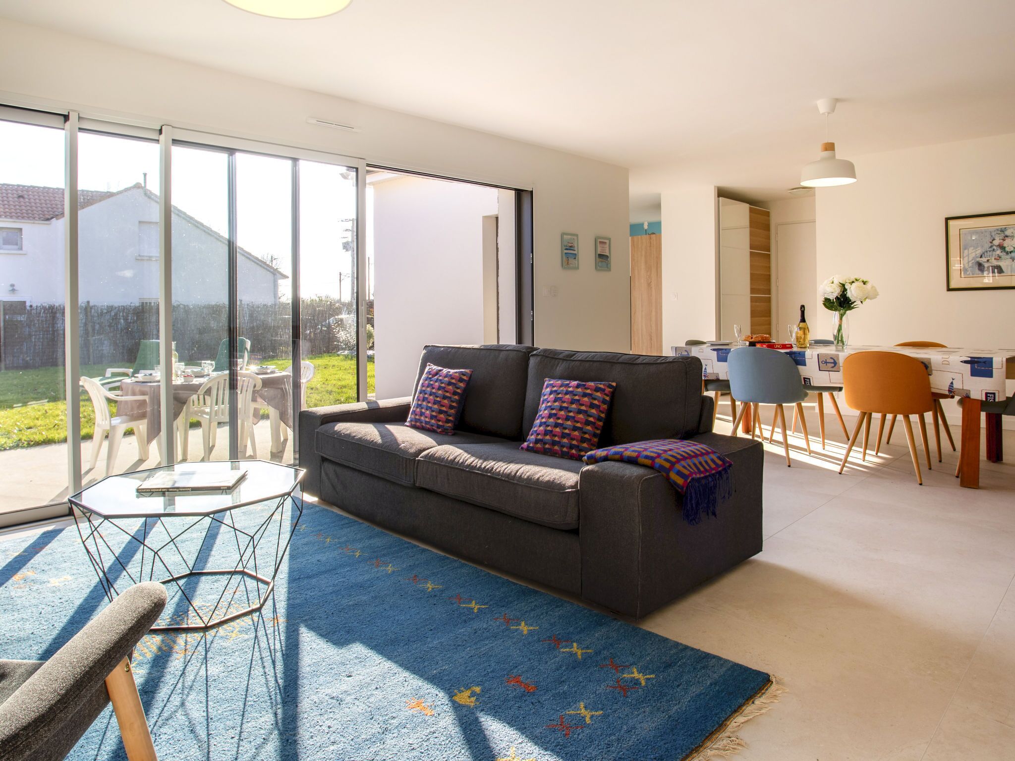 A modern living room with a grey sofa, colorful throw pillows, a glass coffee table, and a blue patterned rug.
