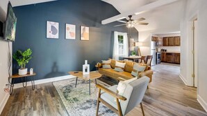 Una sala con una pared de acento azul oscuro, un ventilador de techo, un sofá, una mesa de centro, una mesita auxiliar con una planta y una alfombra.