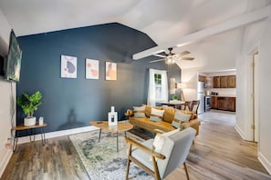 Ein Wohnzimmer mit dunkelblauer Akzentwand, Deckenventilator, Sofa, Couchtisch, Beistelltisch mit Pflanze und Teppich.