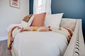 En seng med hvid dyne, flere puder og et beige sengegavl.