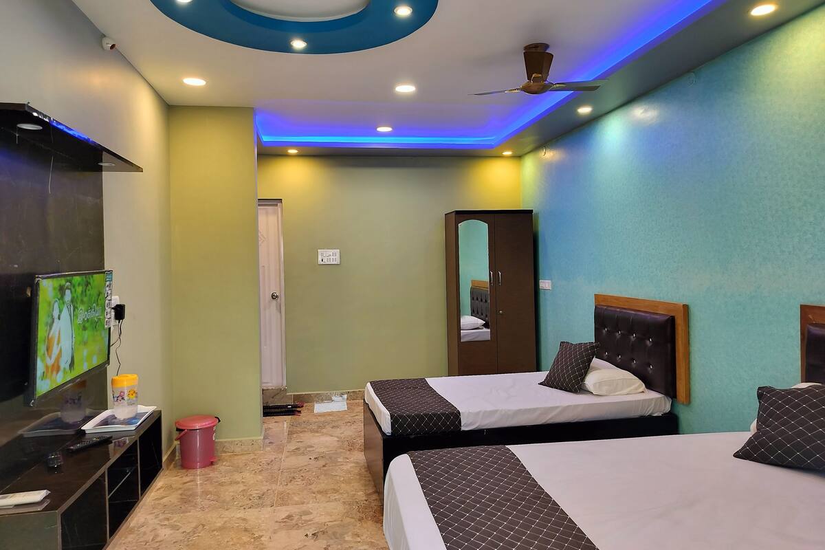 Habitación de hotel con dos camas, televisión, armario y ventilador de techo.