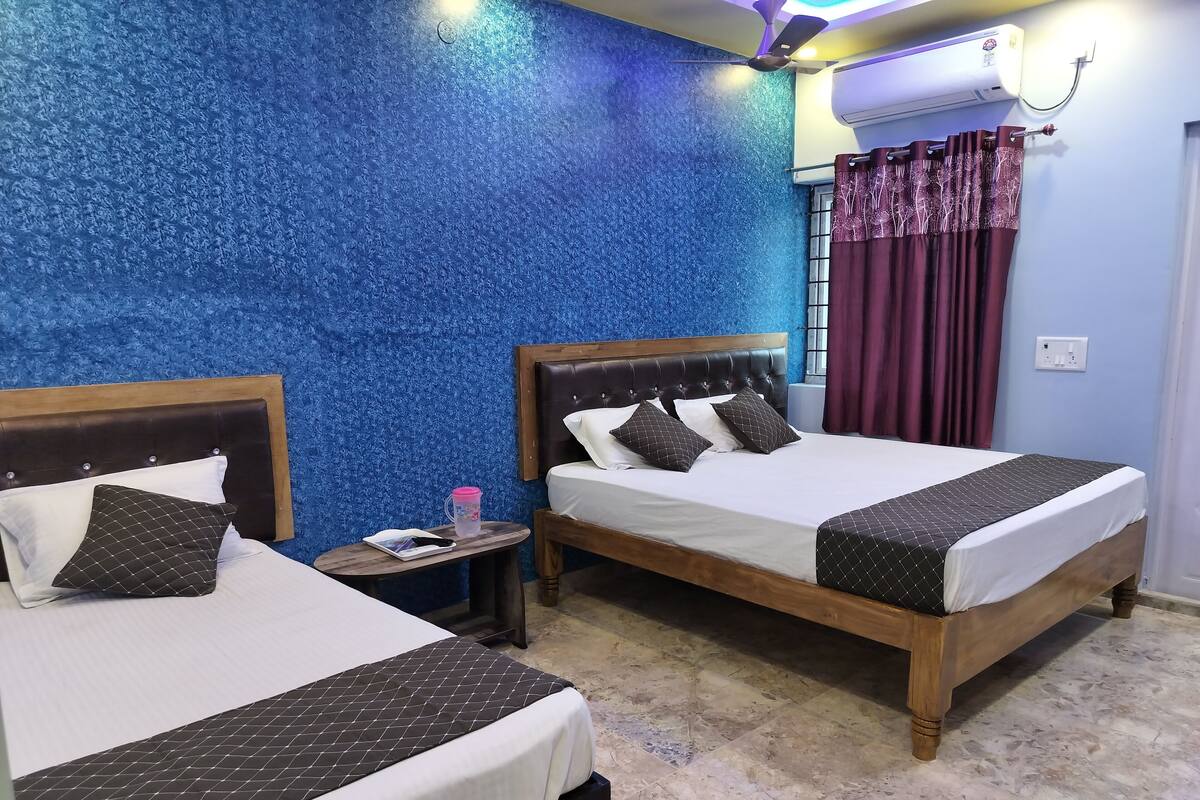 Habitación de hotel con dos camas, una pared azul con textura, un equipo de aire acondicionado y una ventana con cortinas.