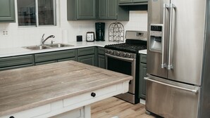 A modern kitchen with green cabinets, a stainless steel refrigerator, a built-in oven, and a wooden island with bar stools.