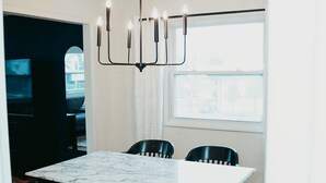 A dining area with a marble table and black chairs, a chandelier, and a window with a view.