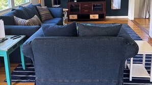 A living room with a dark blue sofa, a wooden coffee table, a ceiling fan, a TV, and a window with blinds.