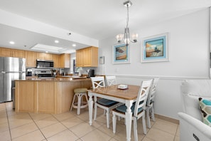 A kitchen with wooden cabinets, a stainless steel refrigerator, and a dining area with a wooden table and white chairs.