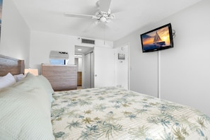 Quarto com cama, ventilador de teto, televisão fixada na parede e porta que dá para outro cômodo.
