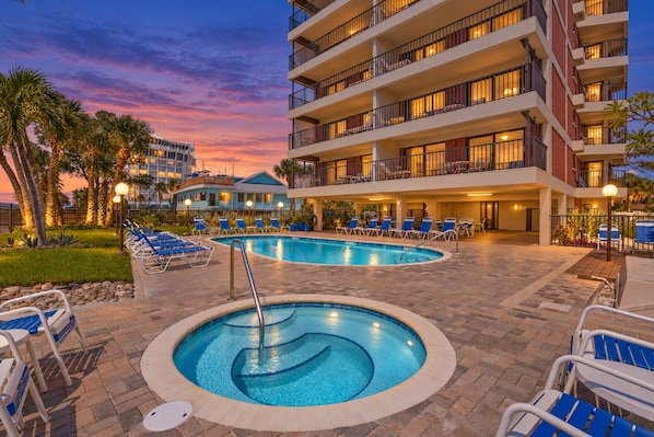 A hotel with a swimming pool, lounge chairs, and a sunset view.
