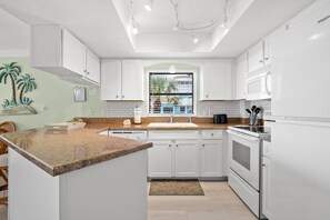 A modern kitchen with white cabinetry, granite countertops, a built-in oven, and a window with blinds.
