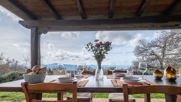 An outdoor dining area with a table set for four, surrounded by wooden chairs. A basket of bread is visible on the table, and a vase with flowers is placed in the center. - Dimora del Re by Interhome (Sassofortino)