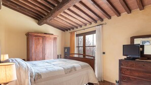 A bedroom with a bed, wooden wardrobe, a dresser, a television, and a window with curtains. - Dimora del Re by Interhome (Sassofortino)