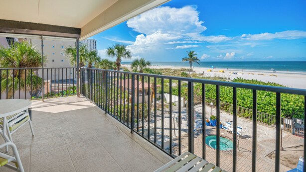 A balcony with a view of a beach, pool, and palm trees.