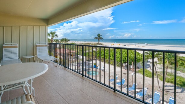 Un balcón con vistas a una playa, una piscina y zona de estar al aire libre.