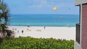 Ein Strand mit klarem, blauem Wasser, einigen Personen und einem Fallschirm in der Ferne.