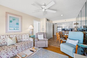 A living room with a sofa, armchair, and a coffee table with remote control and papers. - 🌊 Panoramic Gulf Views & Soothing Coastal Vibes (St Pete Beach)