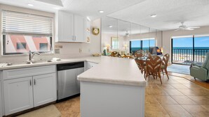 A modern kitchen with a central island, white cabinetry, and a large window overlooking the beach.