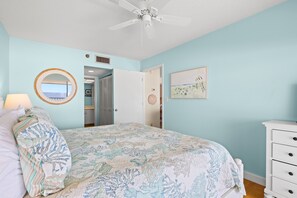 A bedroom with a bed, a bedside table, a mirror, and a ceiling fan. - 🌊 Panoramic Gulf Views & Soothing Coastal Vibes (St Pete Beach)