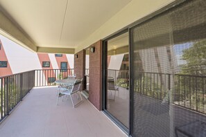 A balcony with a table and chairs, a sliding glass door, and a view of neighboring buildings.